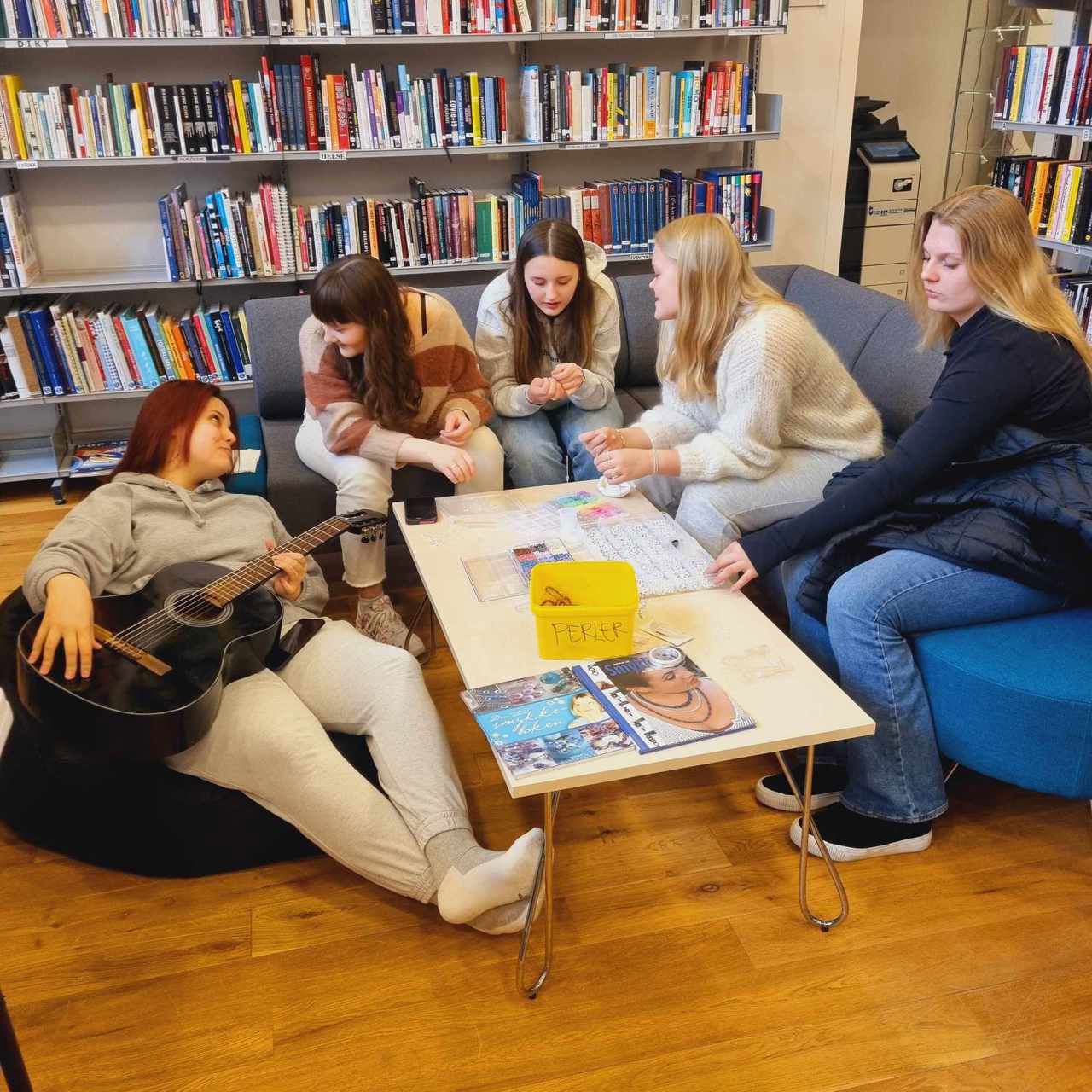 Jenter i sofaen på biblioteket som driv på med perling og ei heldt på ein gitar