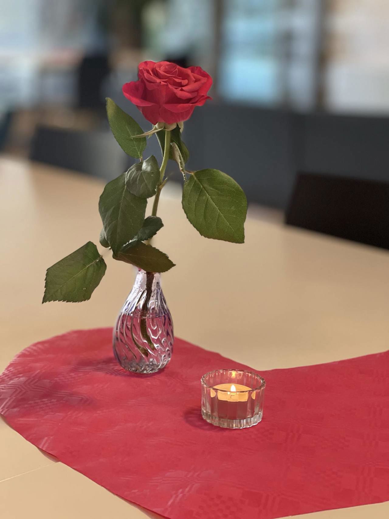 Bilde av eit bord som er pynta med serviett, lys og ei raud rose.